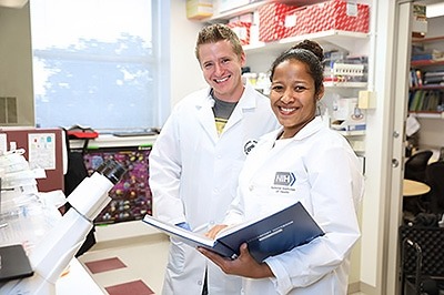 Two scientists in lab coats standing side by side inside a laboratory.