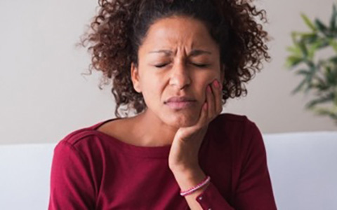 A woman clutches at her jaw in pain.